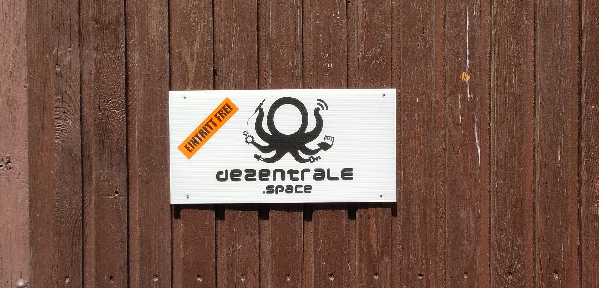 Eine braune HolztÃ¼r mit angebrachtem Schild "dezentrale.space Eintritt Frei"